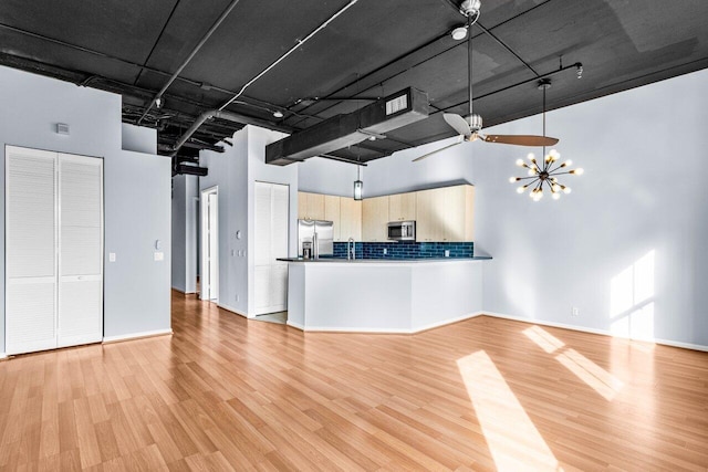 kitchen featuring stainless steel appliances, a high ceiling, light brown cabinetry, and light wood-type flooring