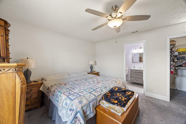 carpeted bedroom with a spacious closet, ceiling fan, ensuite bath, and a closet