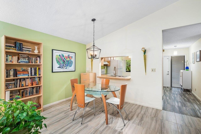 dining area featuring wood-type flooring, vaulted ceiling, an inviting chandelier, a textured ceiling, and sink