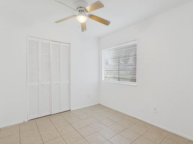 unfurnished bedroom with a closet, a ceiling fan, baseboards, and light tile patterned flooring