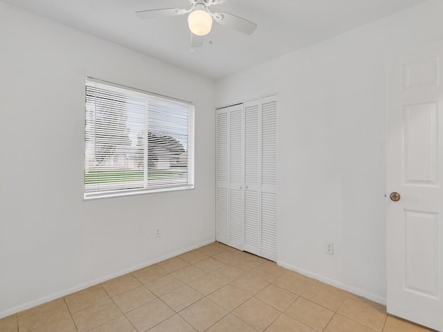 unfurnished bedroom featuring a closet, baseboards, light tile patterned floors, and a ceiling fan