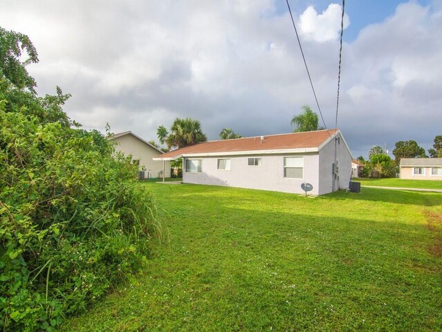 rear view of property featuring cooling unit, a lawn, and stucco siding