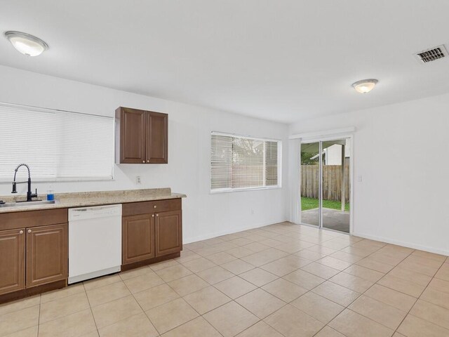 kitchen featuring a sink, dishwasher, light countertops, light tile patterned floors, and baseboards