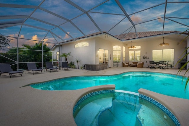 pool at dusk featuring a lanai, ceiling fan, a patio, and an in ground hot tub