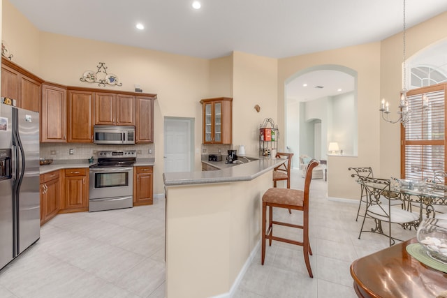 kitchen featuring a kitchen bar, an inviting chandelier, kitchen peninsula, backsplash, and appliances with stainless steel finishes