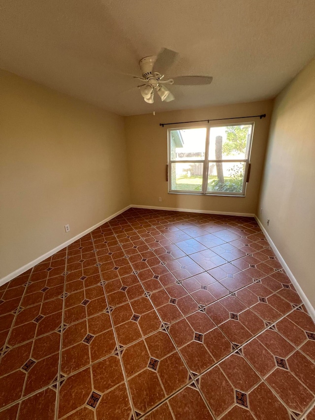 empty room with ceiling fan, a textured ceiling, and dark tile patterned flooring