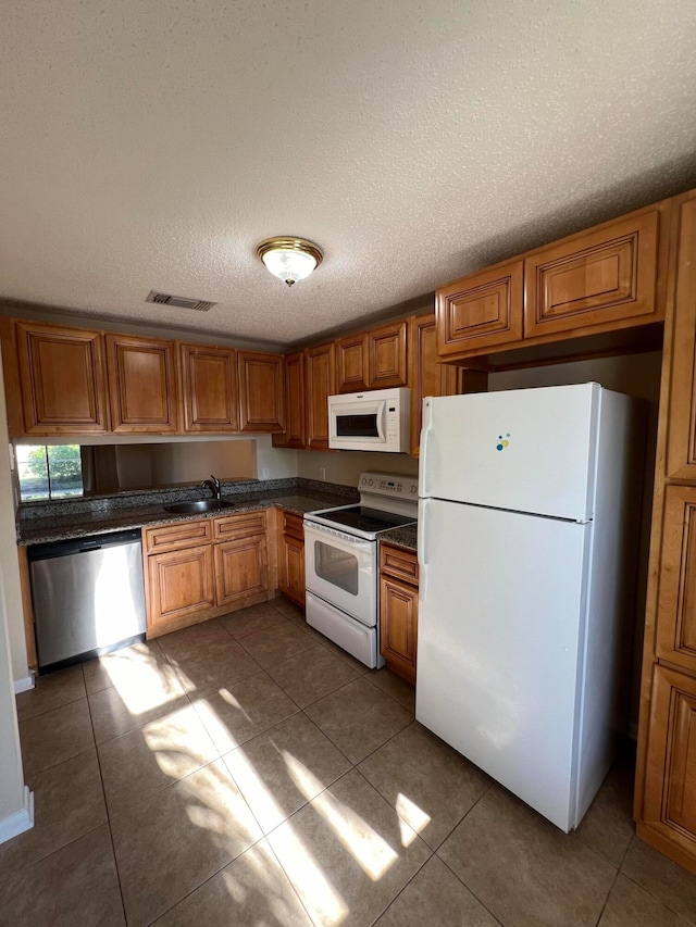 kitchen featuring white appliances, a textured ceiling, sink, and dark tile patterned flooring