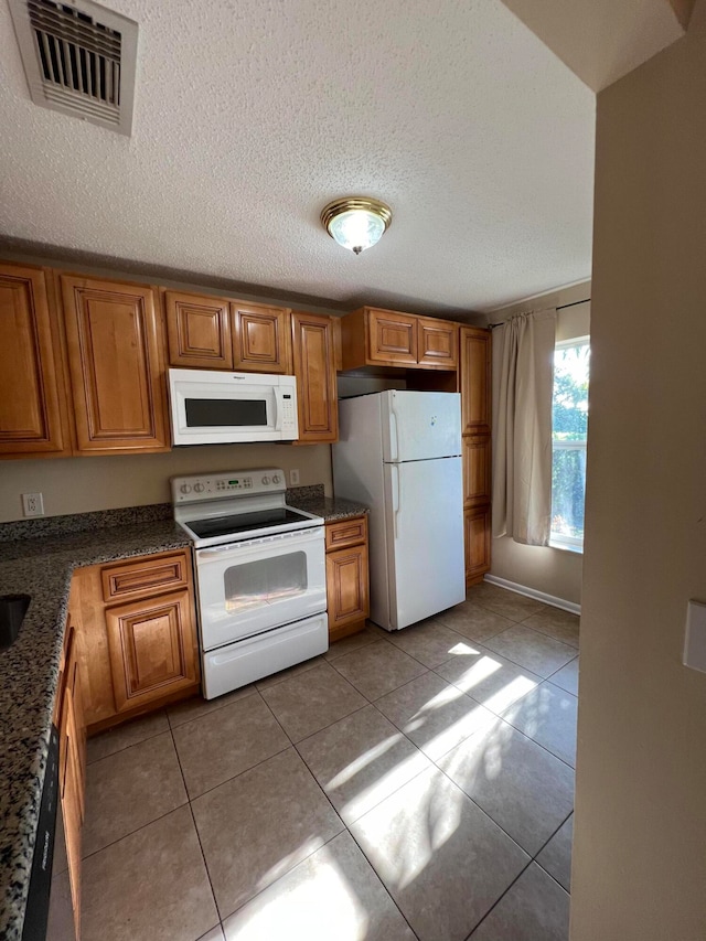 kitchen featuring dark stone counters, white appliances, a textured ceiling, and light tile patterned floors