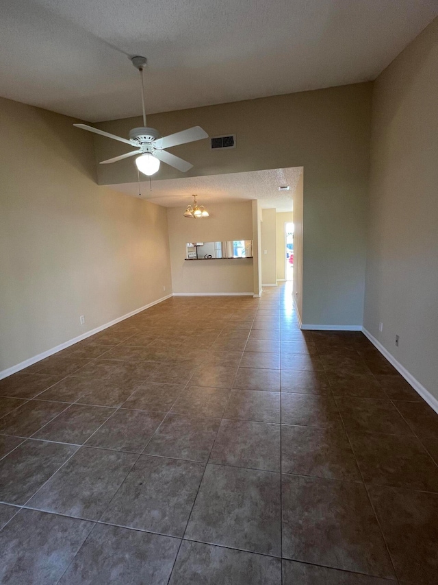 empty room with dark tile patterned flooring, a textured ceiling, and ceiling fan with notable chandelier