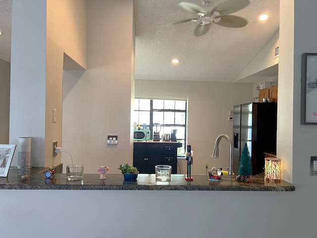 kitchen featuring stainless steel appliances, vaulted ceiling, kitchen peninsula, a textured ceiling, and sink