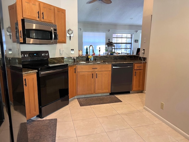 kitchen with sink, appliances with stainless steel finishes, dark stone counters, a textured ceiling, and light tile patterned floors