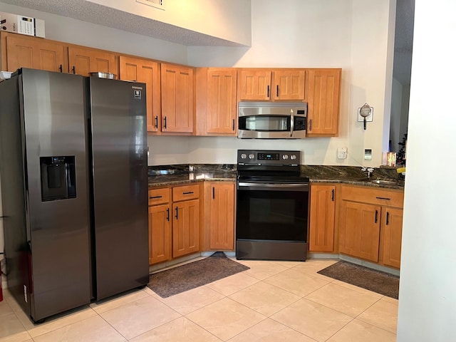 kitchen featuring stainless steel appliances, a textured ceiling, sink, light tile patterned flooring, and dark stone countertops