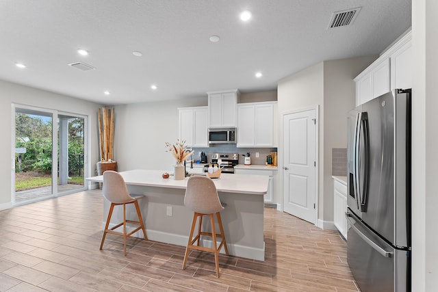 kitchen with a center island with sink, stainless steel appliances, white cabinetry, a kitchen breakfast bar, and light hardwood / wood-style flooring