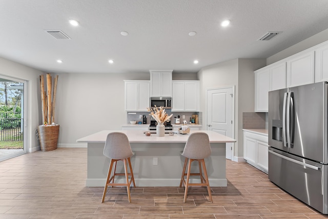 kitchen with white cabinets, a kitchen bar, a center island with sink, and stainless steel appliances