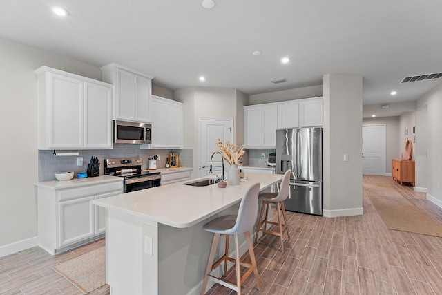 kitchen featuring an island with sink, a breakfast bar area, white cabinetry, and appliances with stainless steel finishes