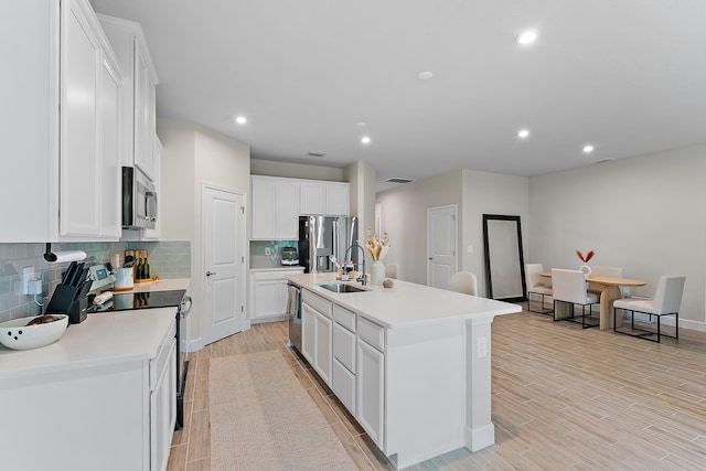 kitchen featuring white cabinets, sink, an island with sink, light wood-type flooring, and appliances with stainless steel finishes