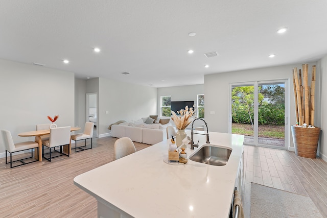 kitchen with a kitchen island with sink, light wood-type flooring, and sink