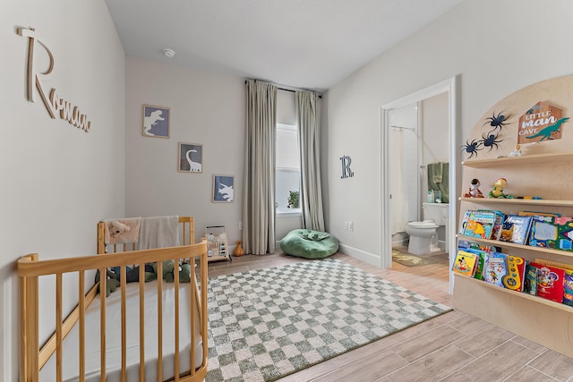 bedroom with a crib, ensuite bath, and wood-type flooring