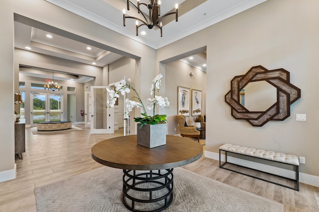 entrance foyer featuring french doors, an inviting chandelier, light hardwood / wood-style floors, a high ceiling, and a tray ceiling