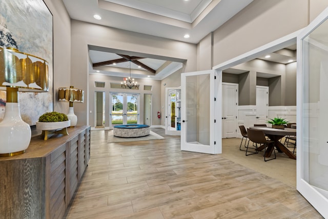 foyer entrance with light hardwood / wood-style floors, a raised ceiling, crown molding, a notable chandelier, and french doors