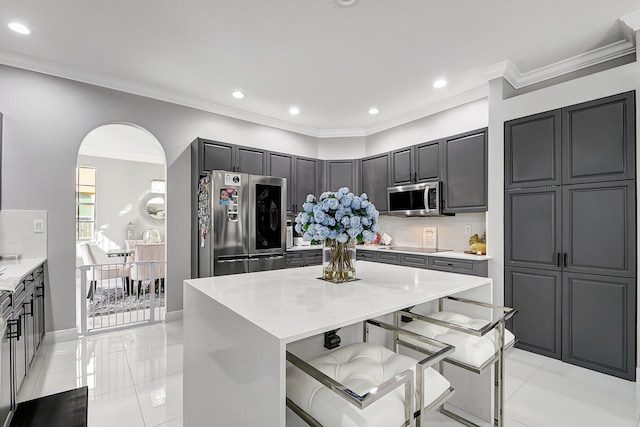 kitchen with appliances with stainless steel finishes, ornamental molding, a breakfast bar area, a kitchen island, and gray cabinets