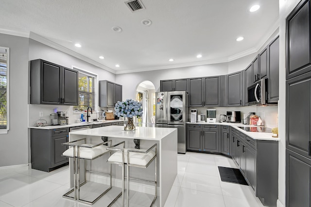 kitchen featuring gray cabinetry, ornamental molding, stainless steel appliances, a breakfast bar, and a center island