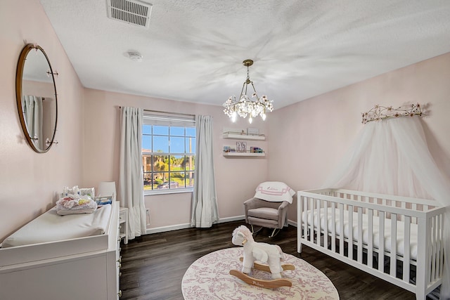 bedroom featuring dark wood-type flooring, a chandelier, a textured ceiling, and a crib