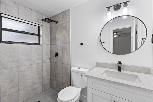 bathroom featuring toilet, ceiling fan, vanity, and a tile shower