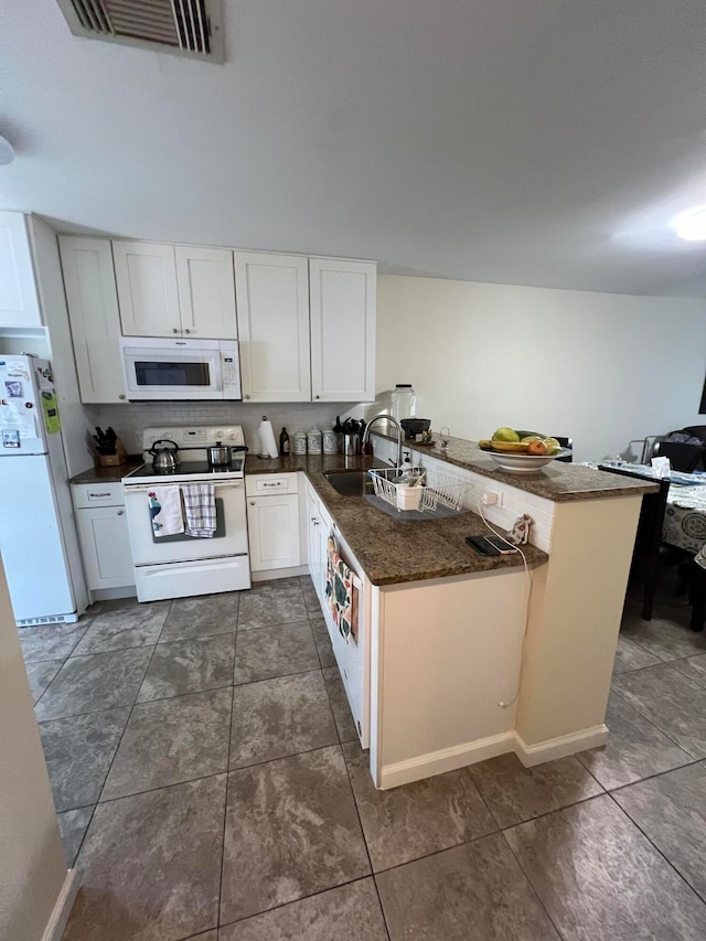 kitchen with dark stone counters, white cabinets, kitchen peninsula, sink, and white appliances