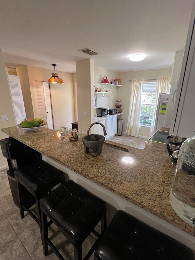 kitchen with light stone counters, white refrigerator, light tile patterned floors, pendant lighting, and a breakfast bar area