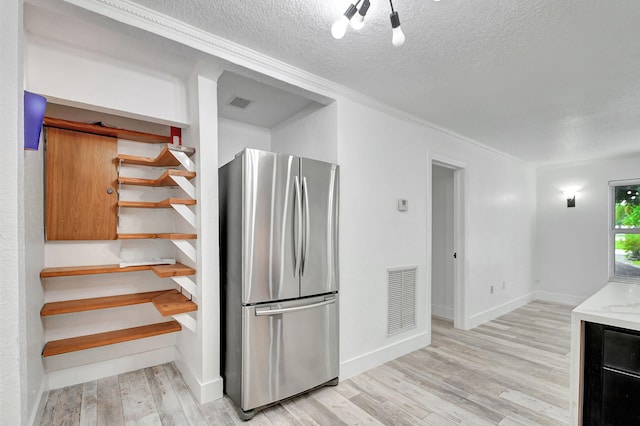 kitchen with a textured ceiling, stainless steel refrigerator, light hardwood / wood-style floors, and crown molding