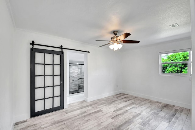 unfurnished room featuring a barn door, ceiling fan, and light hardwood / wood-style flooring