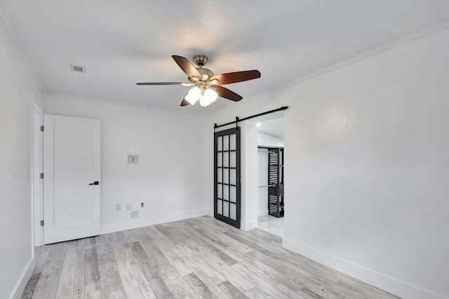 unfurnished room with a barn door, ceiling fan, light wood-type flooring, and crown molding