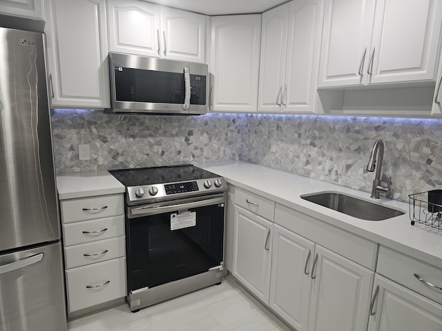 kitchen with stainless steel appliances, a sink, white cabinets, light countertops, and backsplash