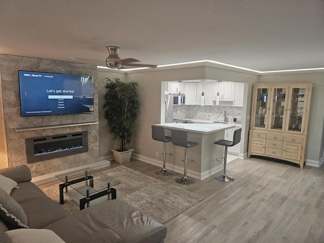 living area with baseboards, a fireplace, light wood finished floors, and ceiling fan