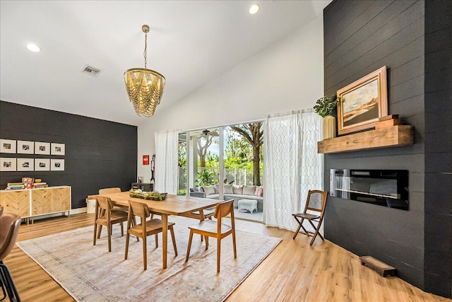 dining room featuring light wood-type flooring, a fireplace, high vaulted ceiling, and an inviting chandelier