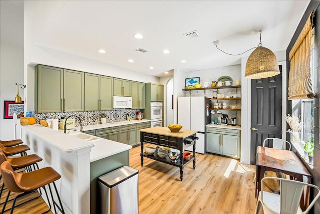 kitchen featuring green cabinets, sink, kitchen peninsula, decorative light fixtures, and white appliances