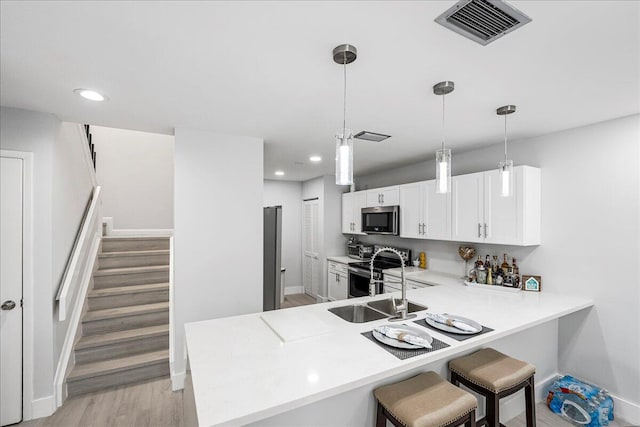 kitchen featuring white cabinets, hanging light fixtures, appliances with stainless steel finishes, light hardwood / wood-style floors, and kitchen peninsula