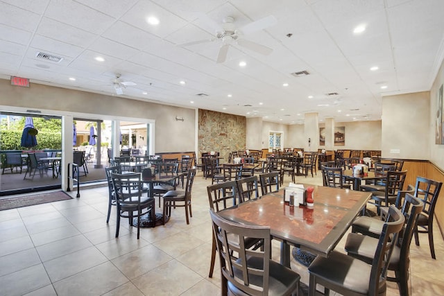 dining space with light tile patterned flooring, wood walls, and ceiling fan