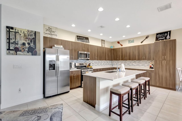 kitchen featuring light tile patterned flooring, appliances with stainless steel finishes, sink, an island with sink, and a kitchen breakfast bar