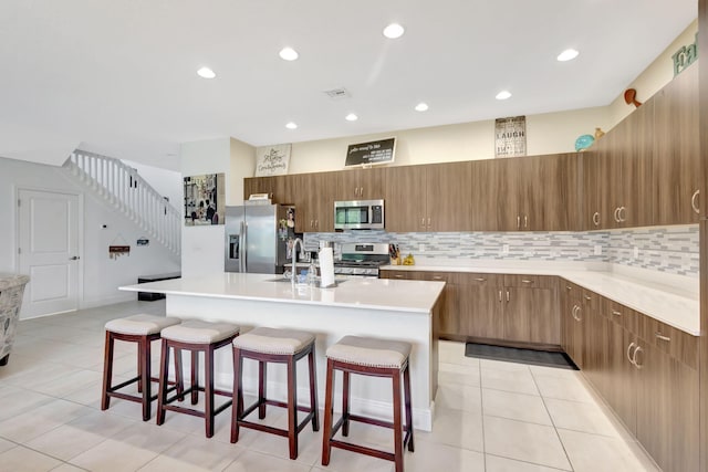 kitchen featuring stainless steel appliances, a center island with sink, sink, a kitchen breakfast bar, and light tile patterned floors