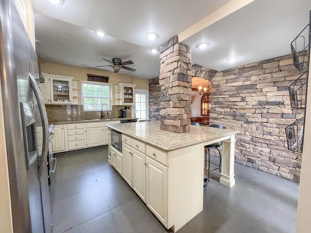 kitchen featuring light stone counters, decorative columns, a kitchen island, backsplash, and appliances with stainless steel finishes