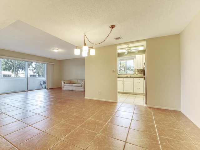 tiled empty room with ceiling fan and a textured ceiling