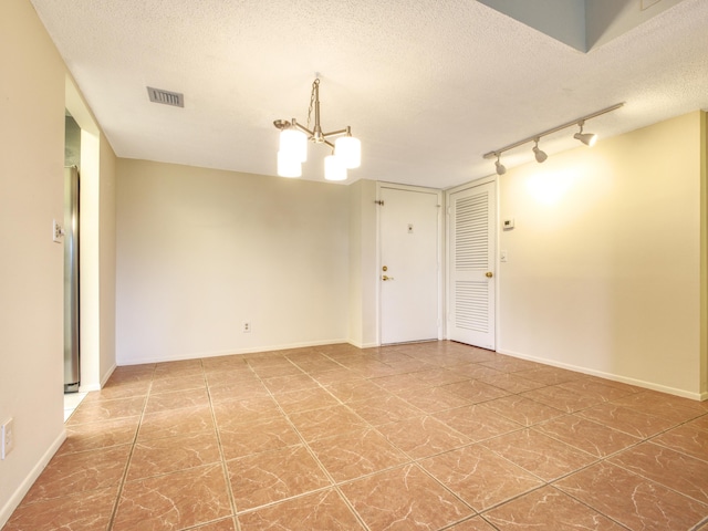 spare room with tile patterned flooring, a notable chandelier, track lighting, and a textured ceiling