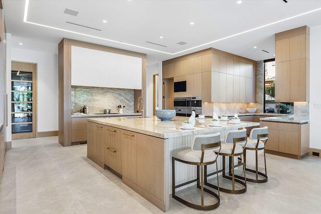 kitchen featuring light brown cabinets, decorative backsplash, and an island with sink