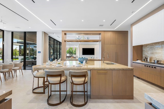 kitchen with light stone countertops, sink, a kitchen breakfast bar, stainless steel gas stovetop, and a spacious island