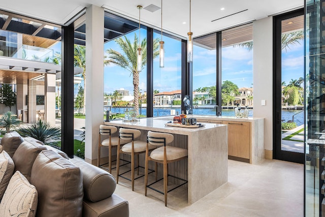 interior space featuring a kitchen island, light brown cabinets, hanging light fixtures, floor to ceiling windows, and a water view