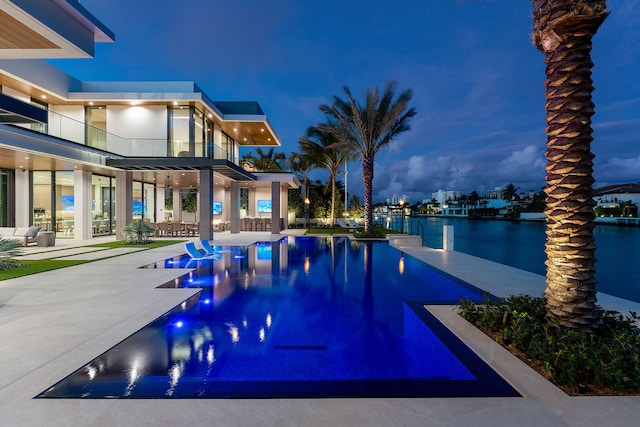 pool at dusk with a water view and a patio area