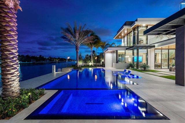 pool at dusk with a patio, a water view, and an in ground hot tub