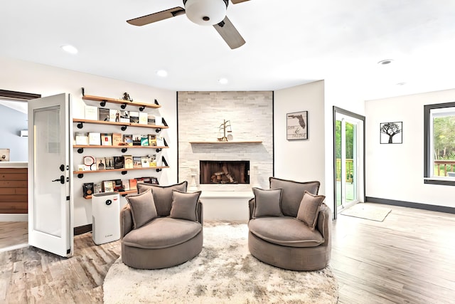 living room with light wood-type flooring, a large fireplace, and ceiling fan